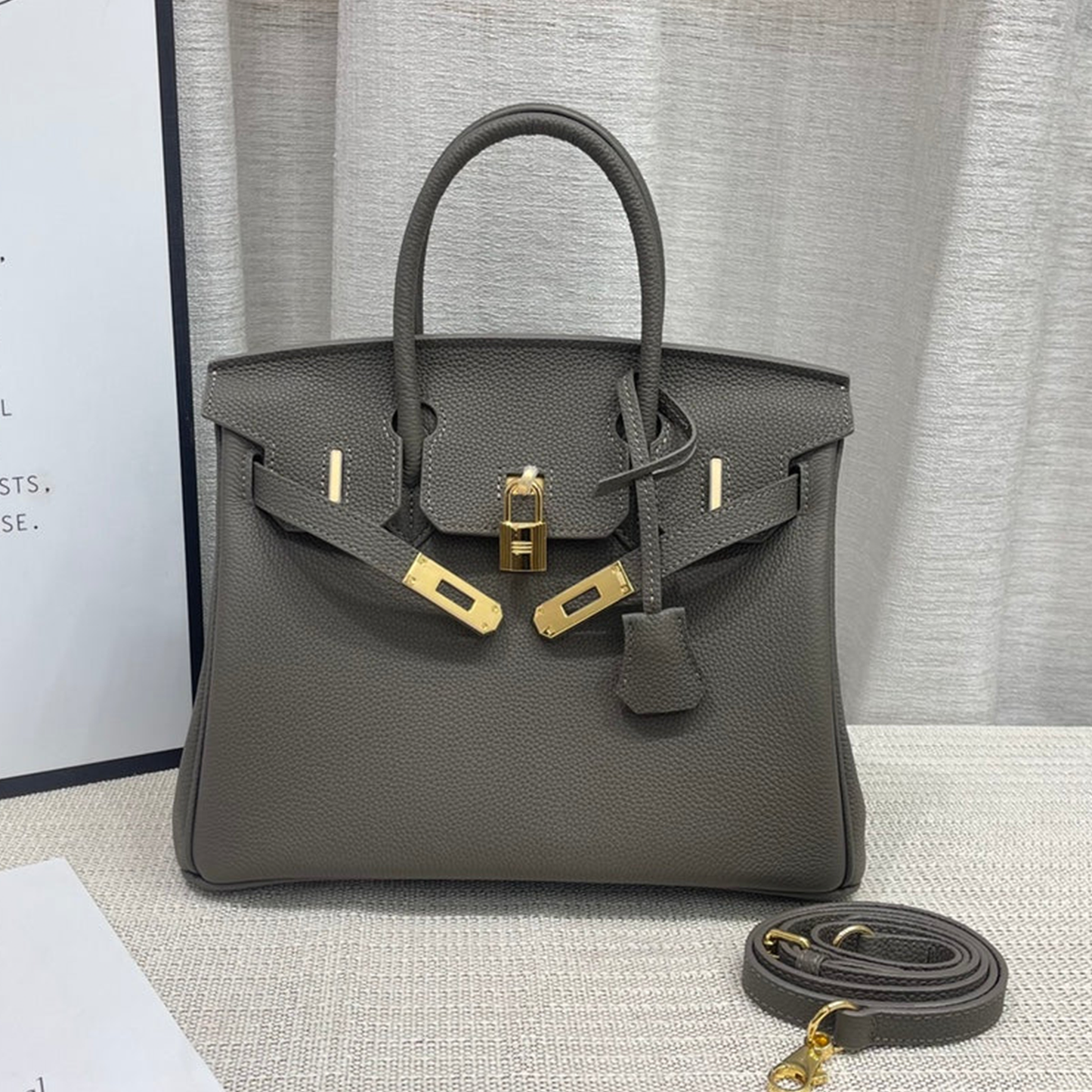 Muted Ash Grey Natural Grain Compact Structured Trapezoid Tote With Glossy Warm Golden Twist Lock Hardware And Tonal Suspended Metal Padlock Charm